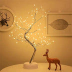 Warm LED Fairy Light Tree Lamp on a round white table beside a small deer figurine and wall art  soft golden illumination creating a peaceful bedroom atmosphere. Bellvian