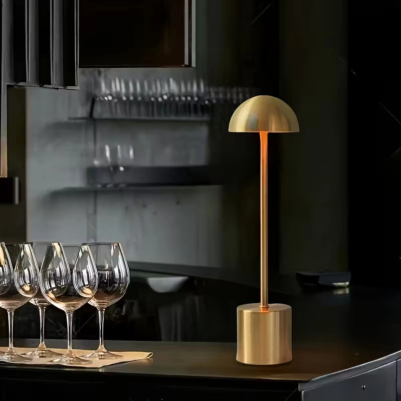 Modern gold LED table lamp illuminating a bar counter beside wine glasses, perfect for restaurants, cafés, and luxury interiors. Bellvian UK contemporary lighting.