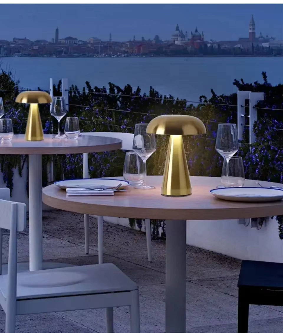 Gold mushroom LED table lamp illuminating an outdoor restaurant setting; rechargeable, cordless and weather-friendly ambience lighting.