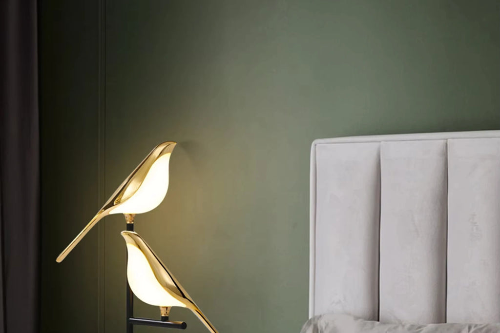 Golden Bellvian bird LED lamp illuminating beside white headboard, elegant modern bedroom decor.