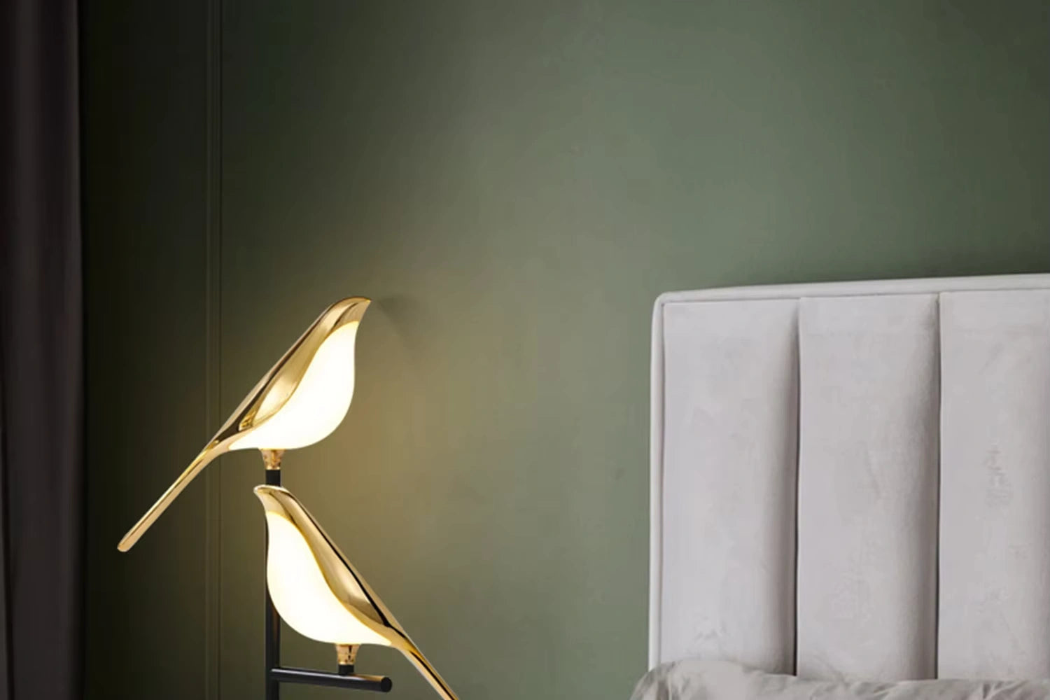 Golden Bellvian bird LED lamp illuminating beside white headboard, elegant modern bedroom decor.