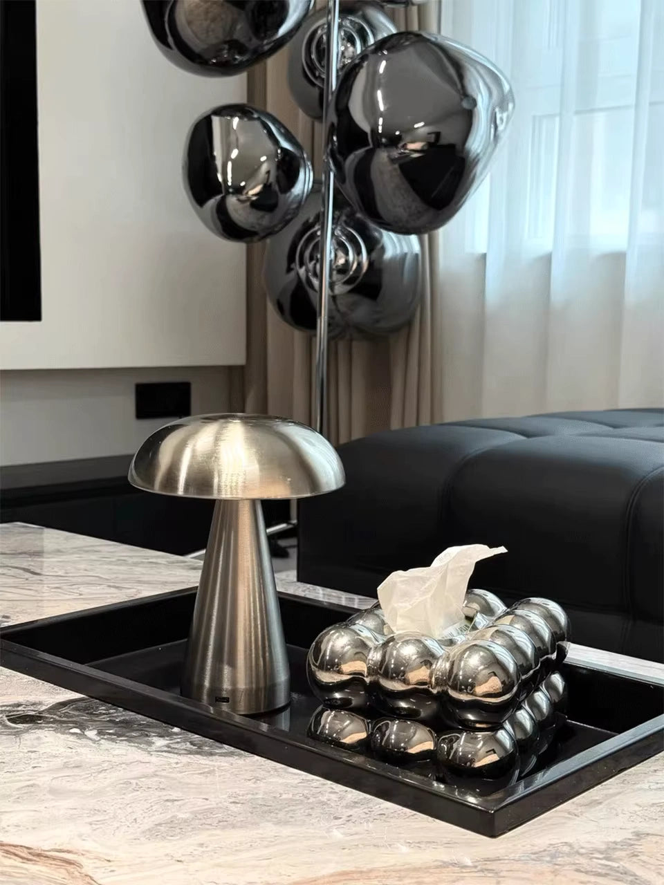 Silver mushroom lamp on a tray in a modern living room; brushed metal, LED, rechargeable and touch-dimmable for stylish décor accents.