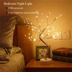 LED Fairy Light Spirit Tree Lamp on a bedside table with vintage books and a framed butterfly art, emitting warm golden glow  USB and battery-powered night lamp for bedrooms. Bellvian