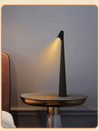 Black minimalist LED bedside lamp emitting soft golden light on a modern round side table next to a bed, creating an elegant nighttime atmosphere. Bellvian