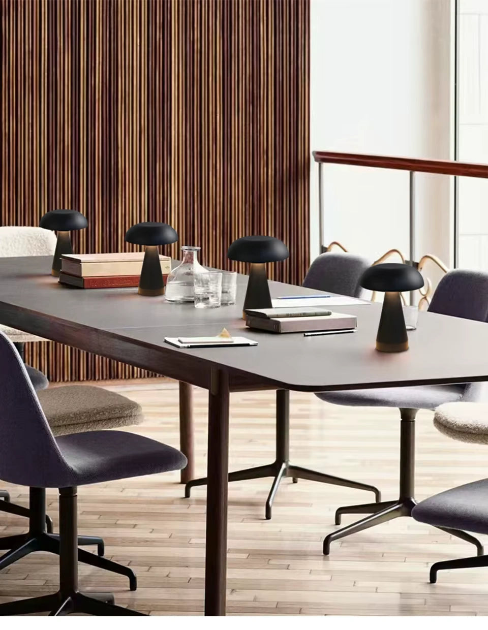 Set of matte black mushroom LED table lamps placed on a modern conference table surrounded by grey chairs. Cordless, rechargeable lamps providing ambient and task lighting for offices, cafés, or meeting spaces.