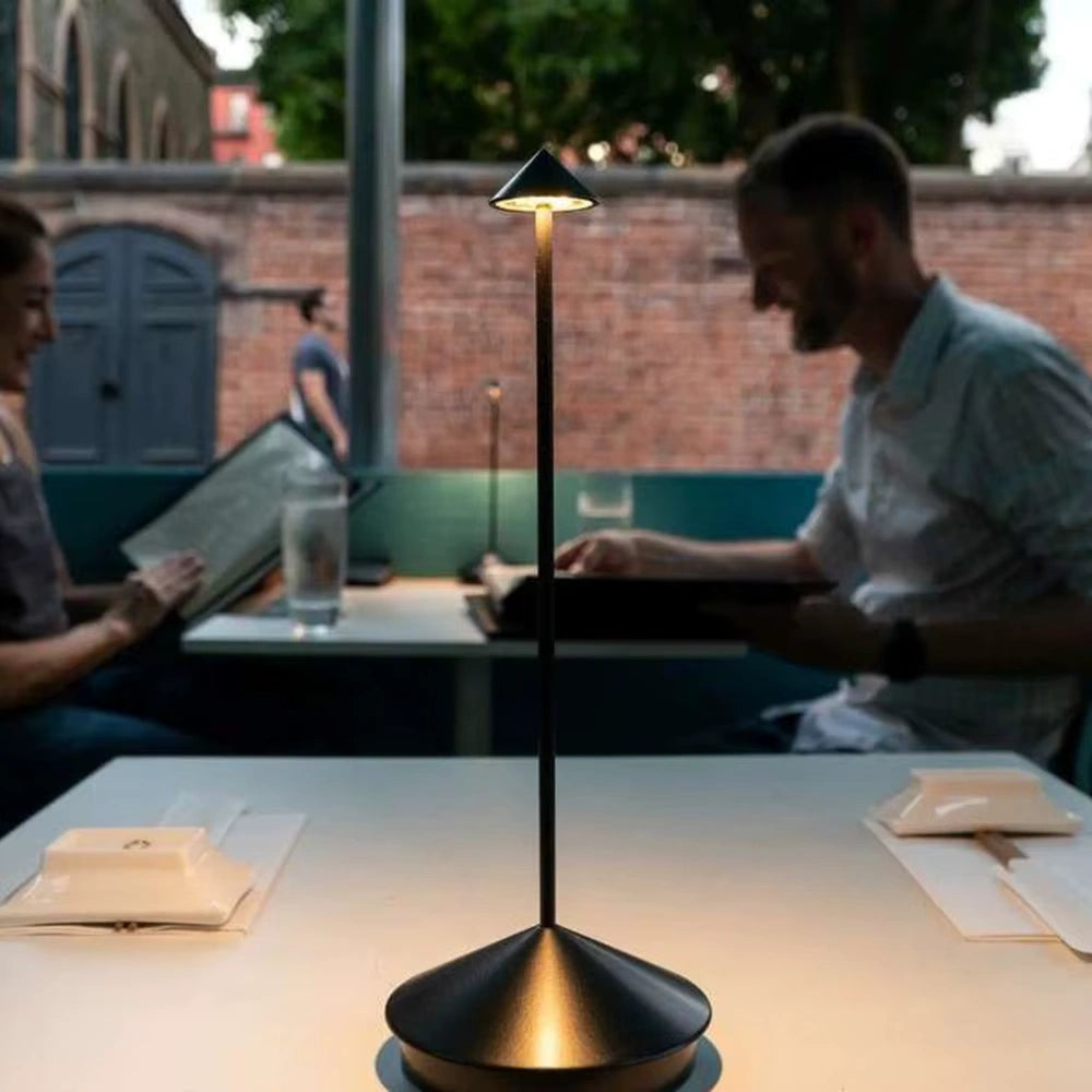Cordless LED table lamp glowing on a restaurant table while two people dine outdoors, creating a warm and intimate evening ambiance.