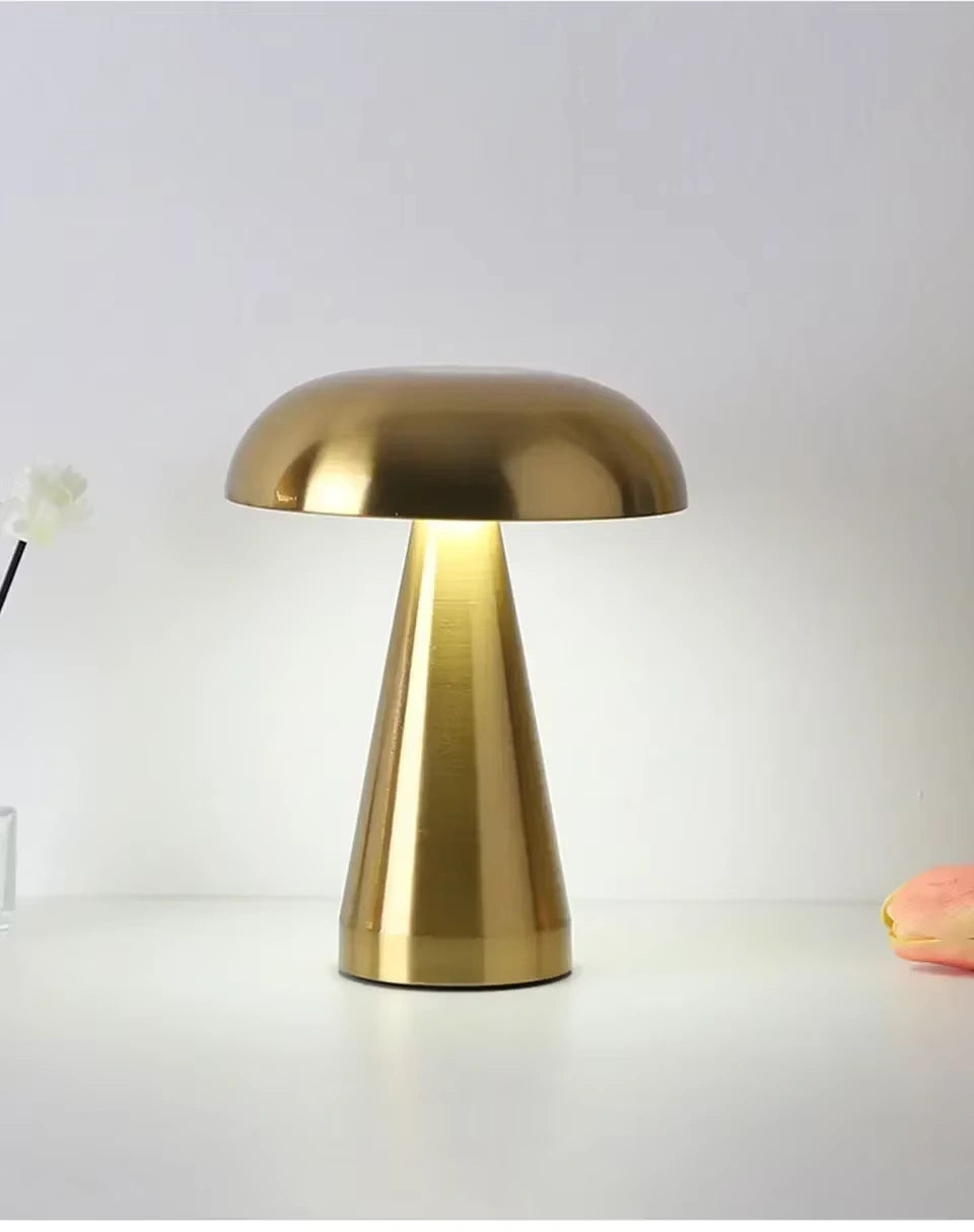 Gold mushroom LED lamp standing on a white surface, emitting soft warm light. Minimalist and rechargeable design perfect for bedside tables, living rooms, or office lighting. Dimmable touch control for elegant modern décor.