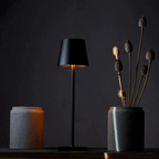 Black LED table lamp emitting a soft warm light in a dark modern interior. Ideal for night ambiance, reading, or decorative lighting in contemporary spaces.