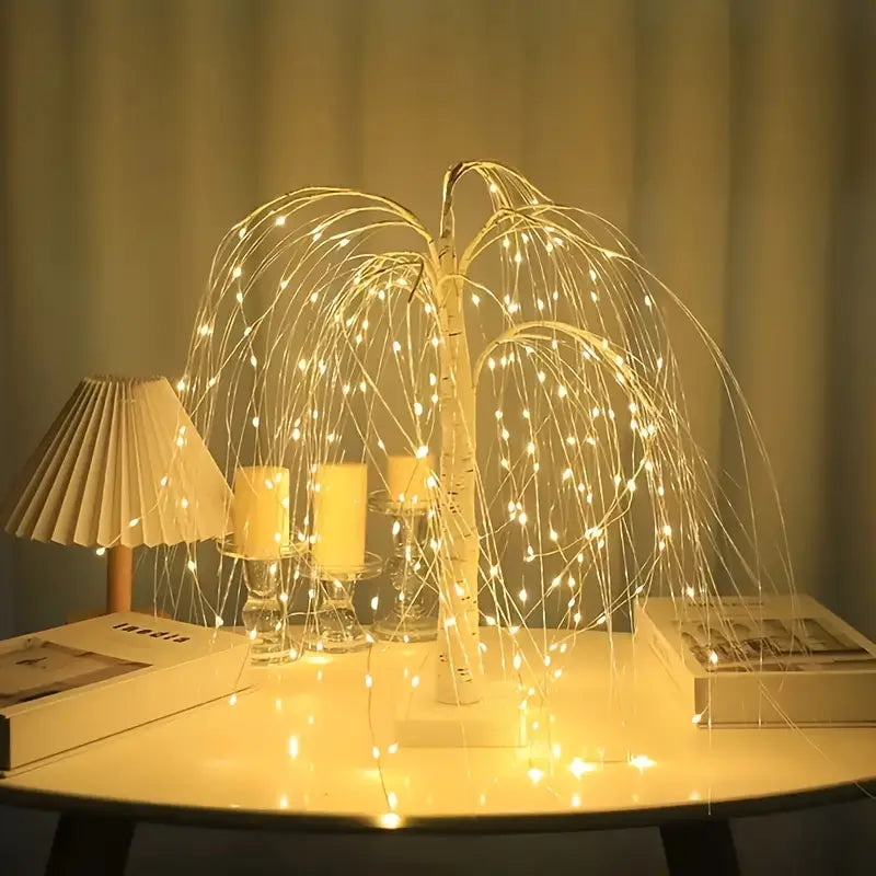 Bright LED tree lamp with cascading warm lights displayed on a white table beside candles and decorative objects. The glowing branches spread soft golden light across the surface, enhancing a modern and elegant room ambiance.Bellvian