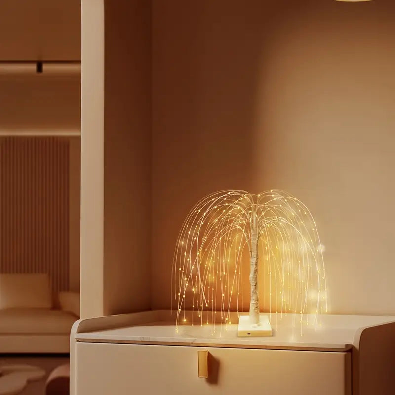 Minimalist LED willow tree lamp placed on a light-colored cabinet in a modern home interior. The cascading golden fairy lights create a warm and inviting glow, ideal for elegant living spaces and cozy nighttime ambiance.