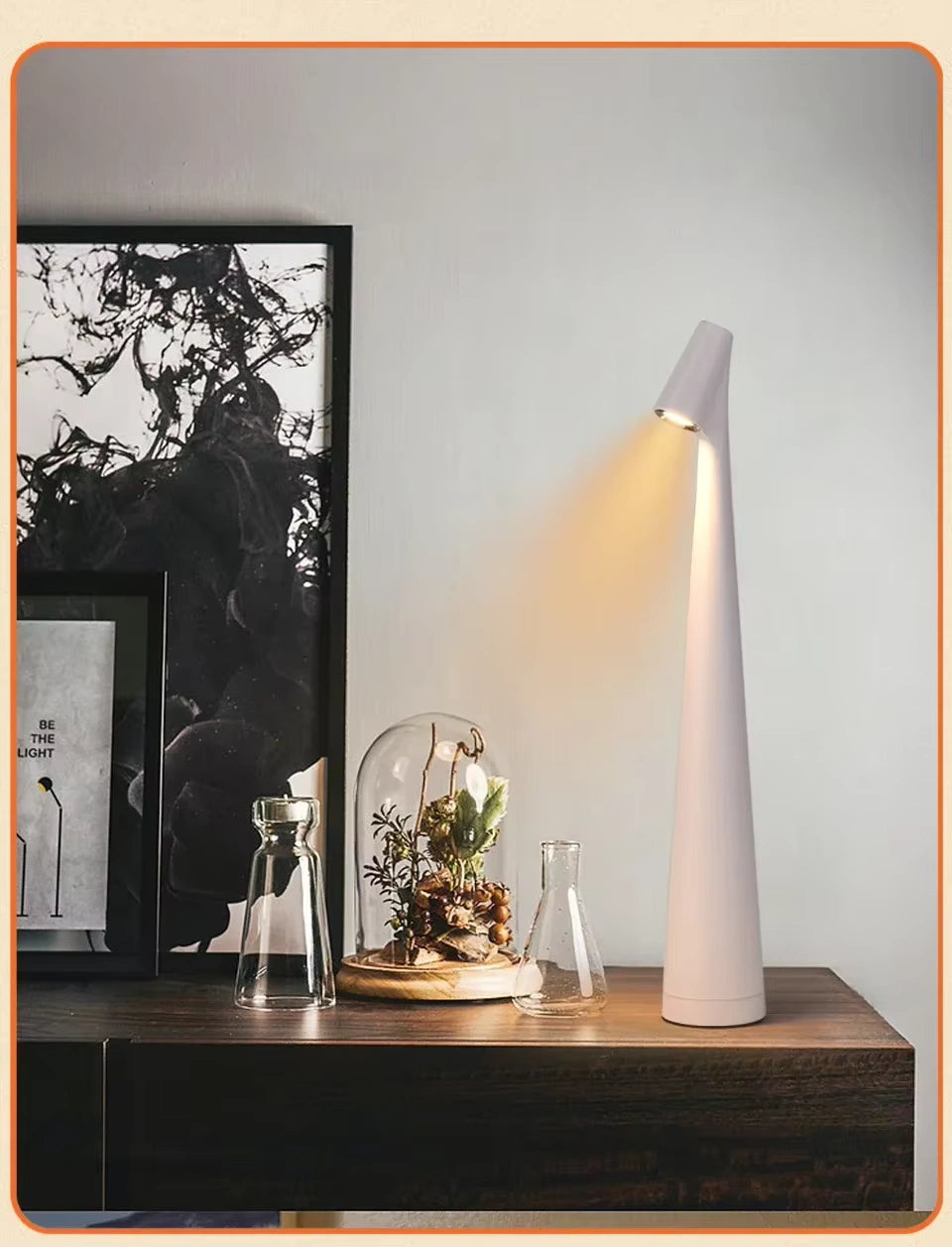 Minimalist LED desk lamp placed on a dark wooden shelf beside glass decor and a terrarium. The soft warm light enhances the cozy, natural home decor ambiance. Bellvian