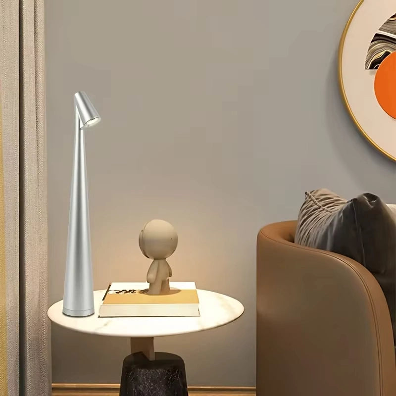 Silver metallic LED table lamp placed on a round marble side table beside a beige sofa and abstract wall art, enhancing contemporary living room decor. Bellvian