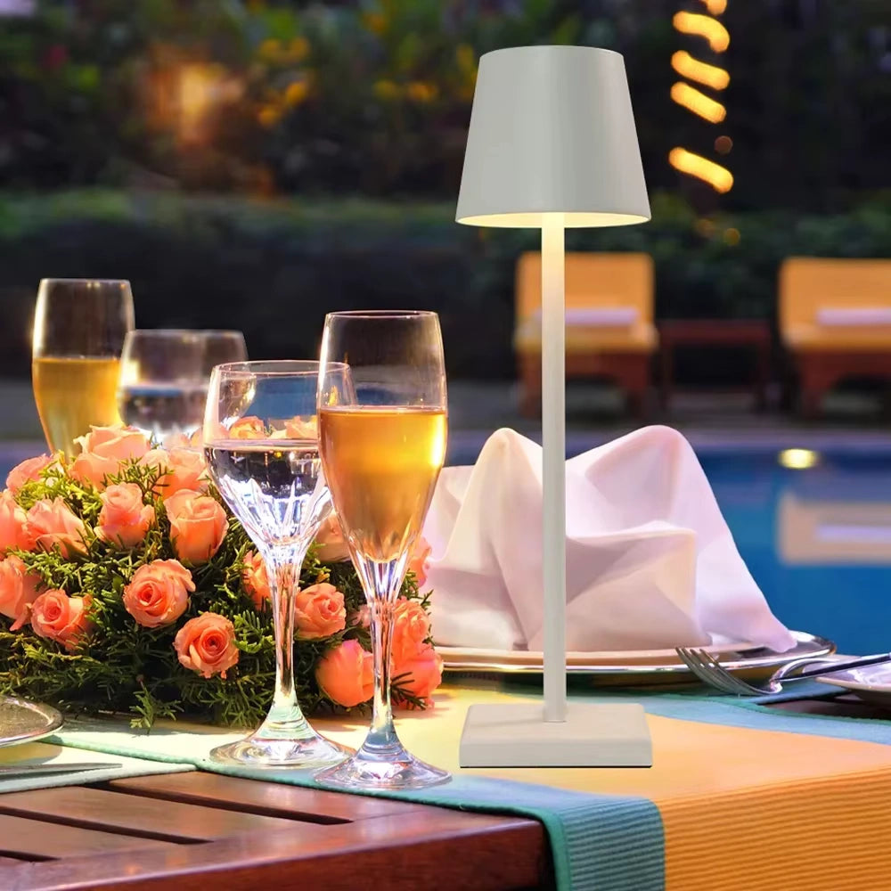 White rechargeable LED table lamp illuminating an elegant outdoor dining setup with glasses and flowers. Perfect for restaurants, garden parties, and romantic evening décor.