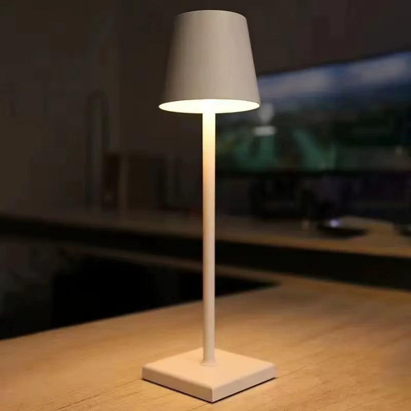 White rechargeable LED table lamp with a slim minimalist design, illuminating a modern desk setup. Ideal for bedroom, office, or living room lighting. Soft warm glow creates a relaxing atmosphere.